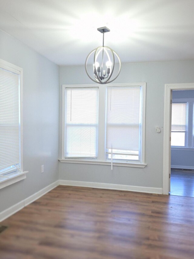 unfurnished dining area featuring an inviting chandelier, wood finished floors, and baseboards