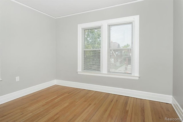 spare room featuring baseboards, light wood-type flooring, and crown molding