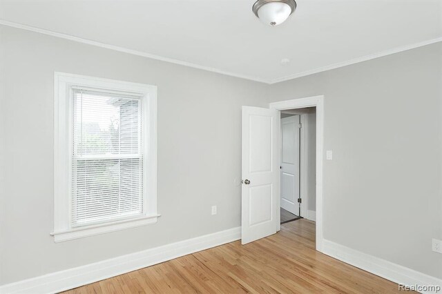 spare room with baseboards, ornamental molding, and light wood finished floors