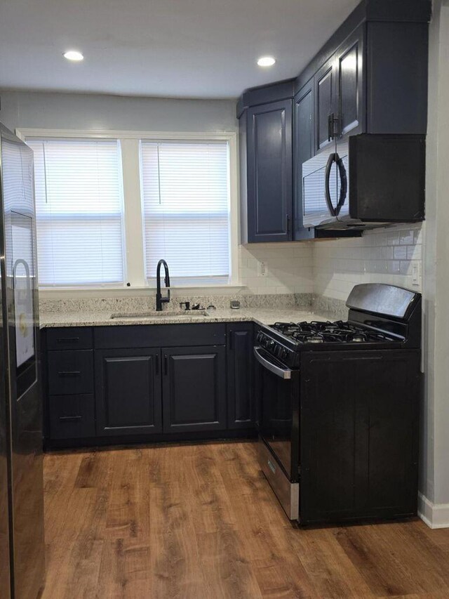 kitchen featuring light stone countertops, black appliances, dark wood-style flooring, and a sink
