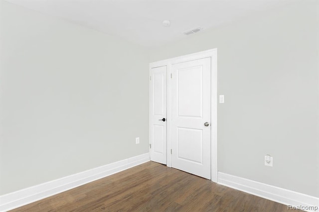 spare room featuring dark wood-type flooring, visible vents, and baseboards