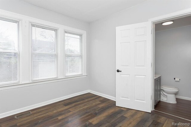 unfurnished bedroom featuring dark wood finished floors, visible vents, connected bathroom, and baseboards