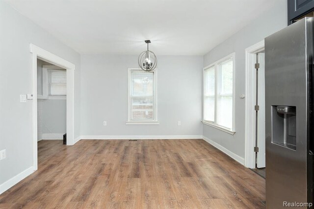 unfurnished dining area featuring baseboards, wood finished floors, and a notable chandelier