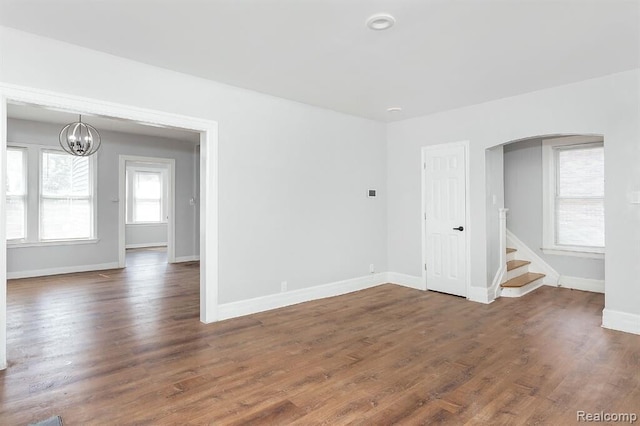 empty room featuring arched walkways, an inviting chandelier, wood finished floors, baseboards, and stairway