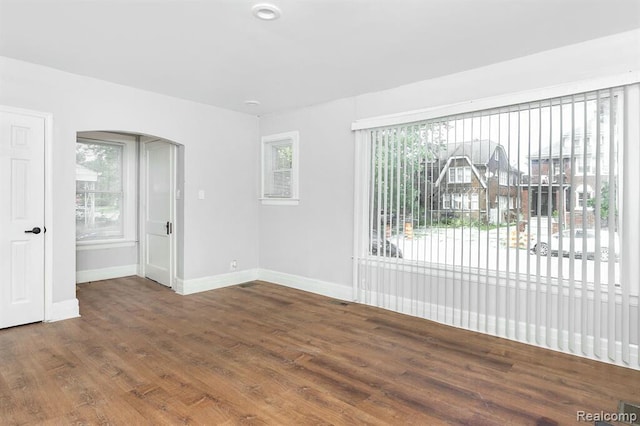 unfurnished living room with baseboards, wood finished floors, and arched walkways