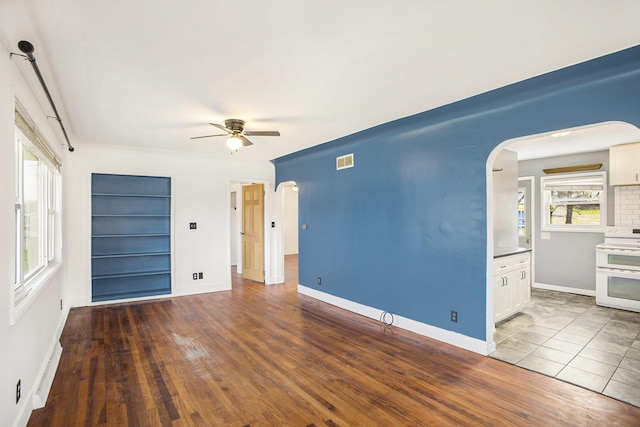 spare room featuring arched walkways, wood finished floors, baseboards, visible vents, and a ceiling fan