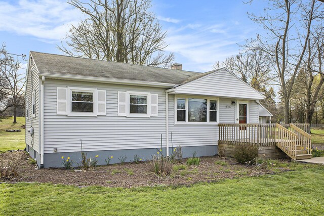 view of front of house with a chimney, a wooden deck, a front lawn, and roof with shingles