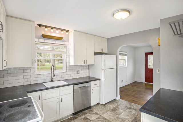 kitchen featuring stainless steel dishwasher, a sink, dark countertops, freestanding refrigerator, and arched walkways