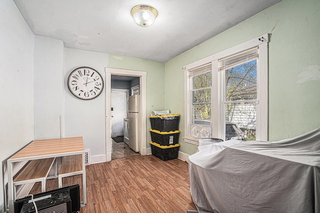 bedroom featuring freestanding refrigerator, wood finished floors, and baseboards