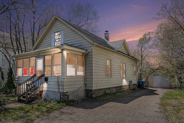 view of front facade featuring driveway, an outdoor structure, a chimney, a detached garage, and a sunroom