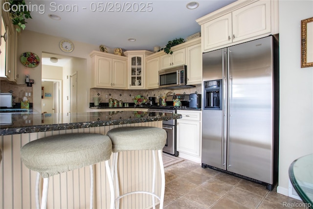 140 Indian Knolls St, Oxford, MI 48371 - kitchen with appliances with stainless steel finishes, cream cabinets, decorative backsplash, glass insert cabinets, and a kitchen breakfast bar