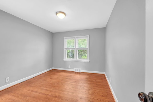 empty room with visible vents, light wood finished floors, and baseboards