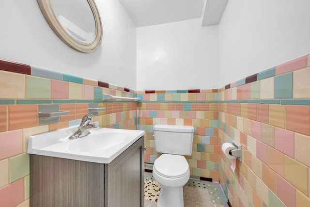 bathroom featuring vanity, a wainscoted wall, toilet, and tile walls