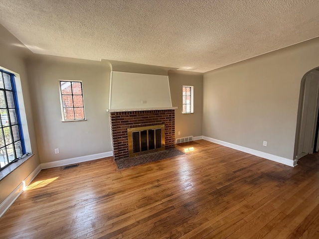 unfurnished living room featuring hardwood / wood-style floors, visible vents, a textured ceiling, and a fireplace