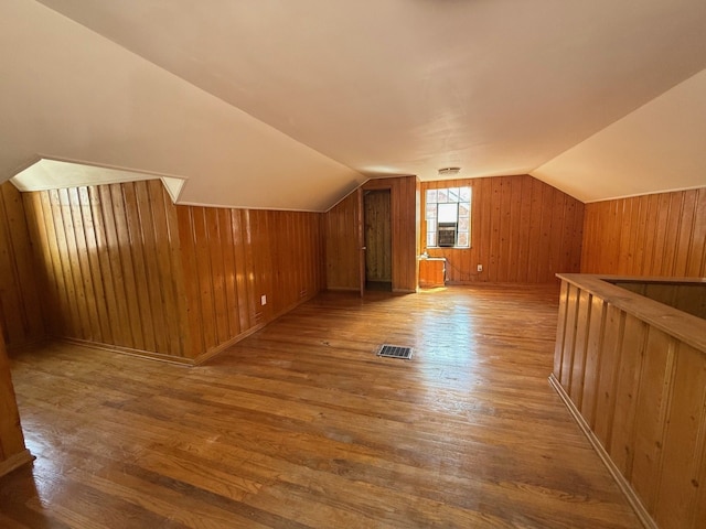 bonus room with wood walls, visible vents, vaulted ceiling, and wood finished floors