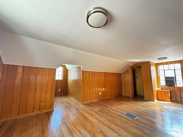 additional living space featuring light wood-style floors, visible vents, wooden walls, and lofted ceiling