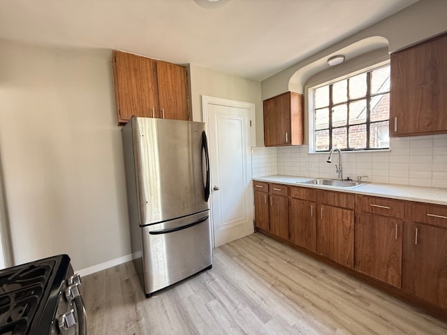 kitchen featuring brown cabinets, a sink, light wood-type flooring, light countertops, and appliances with stainless steel finishes