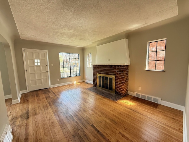 unfurnished living room featuring a brick fireplace, visible vents, baseboards, a textured ceiling, and wood finished floors