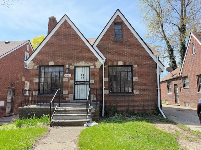 view of front facade featuring brick siding, a front lawn, and a chimney