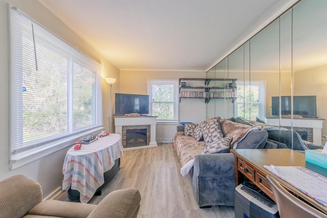living area with ornamental molding, a stone fireplace, baseboards, and light wood-style floors