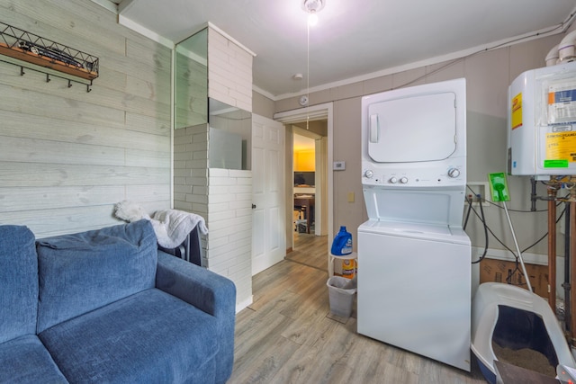 clothes washing area featuring light wood finished floors, stacked washer and clothes dryer, laundry area, wooden walls, and water heater