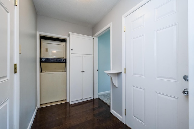 corridor featuring baseboards, stacked washing maching and dryer, and dark wood-type flooring