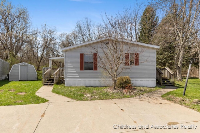 manufactured / mobile home with stairway, a front lawn, a shed, and an outbuilding