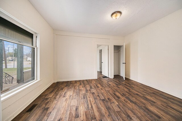 unfurnished room with a textured ceiling, visible vents, dark wood finished floors, and baseboards