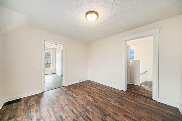 unfurnished room with dark wood finished floors, visible vents, a textured ceiling, and baseboards