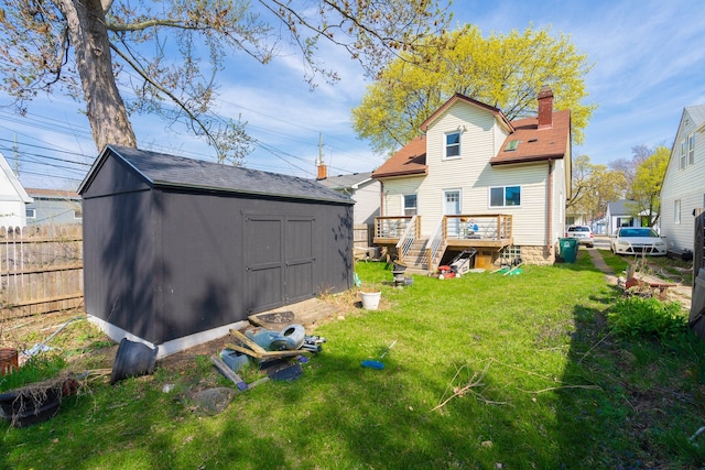 rear view of property with an outdoor structure, fence, a storage shed, a wooden deck, and a lawn