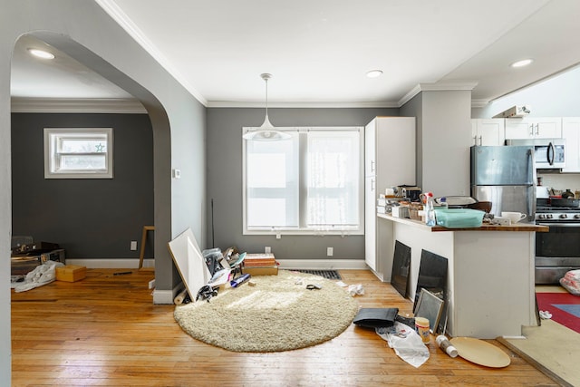 interior space with light wood-style floors, ornamental molding, arched walkways, white cabinets, and appliances with stainless steel finishes