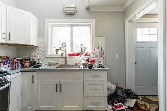 kitchen with light countertops, ornamental molding, backsplash, a sink, and white cabinetry