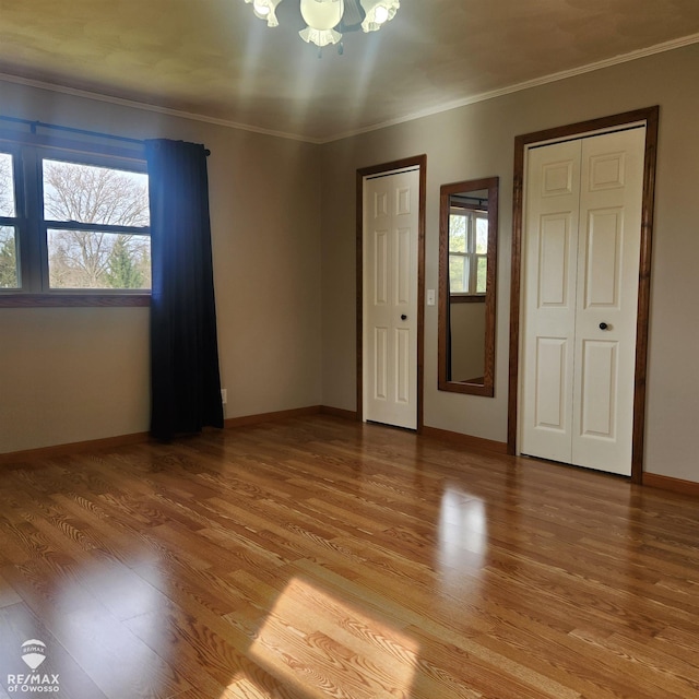 interior space with a notable chandelier, two closets, baseboards, light wood-type flooring, and ornamental molding