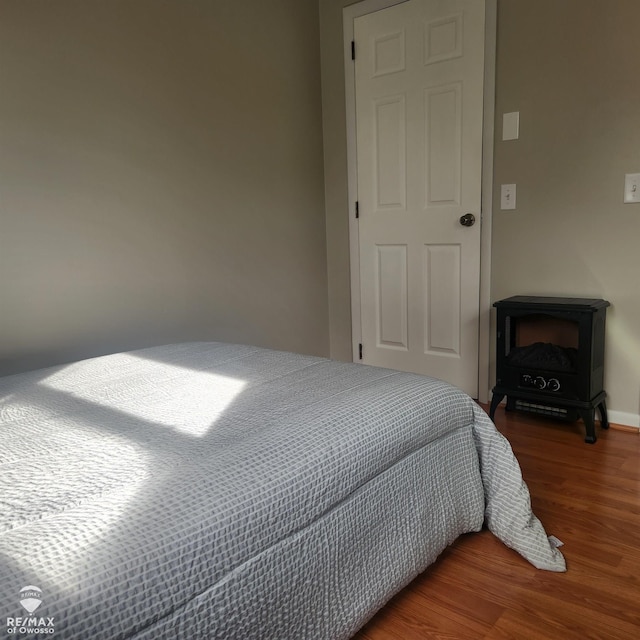 bedroom with baseboards, wood finished floors, and a wood stove