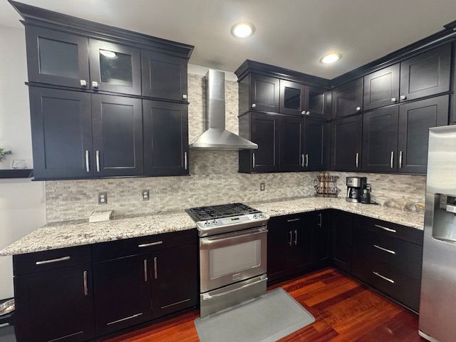 kitchen featuring dark wood-style floors, backsplash, wall chimney exhaust hood, and appliances with stainless steel finishes