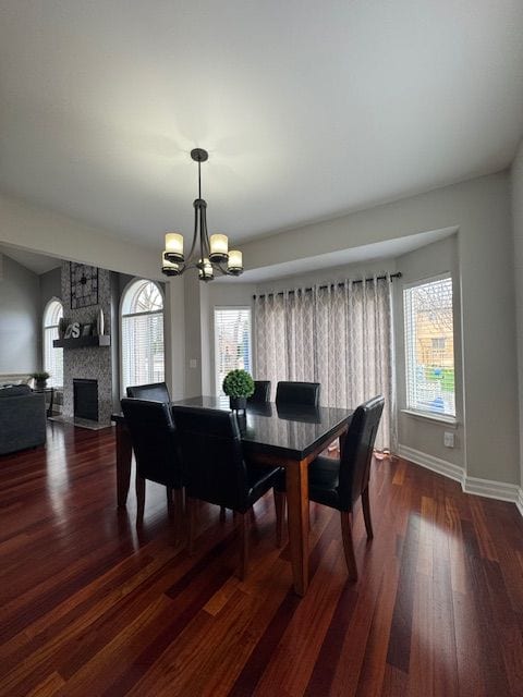 dining room with dark wood finished floors, baseboards, a notable chandelier, and a stone fireplace