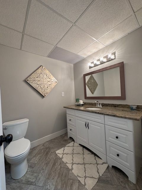 bathroom featuring toilet, a drop ceiling, vanity, and baseboards