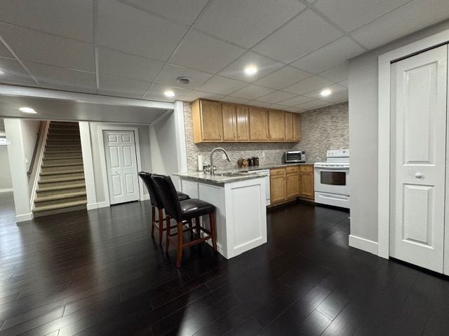 kitchen with a breakfast bar area, a sink, baseboards, white electric stove, and a peninsula