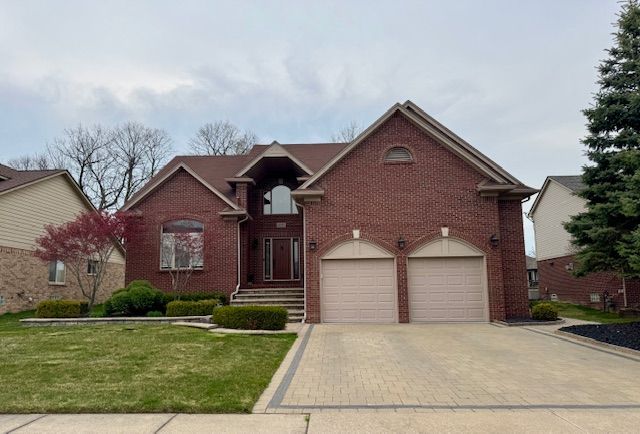 traditional home with brick siding, a front yard, driveway, and an attached garage