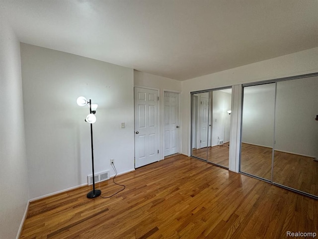 unfurnished bedroom with visible vents, multiple closets, wood finished floors, and baseboards