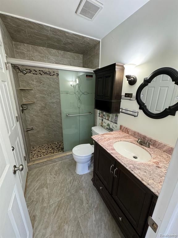 full bathroom featuring toilet, visible vents, a shower stall, and vanity