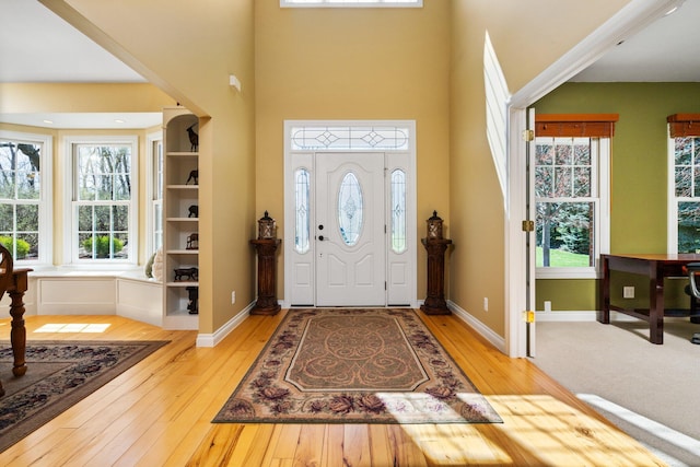 entrance foyer featuring baseboards, light wood-style floors, and a towering ceiling