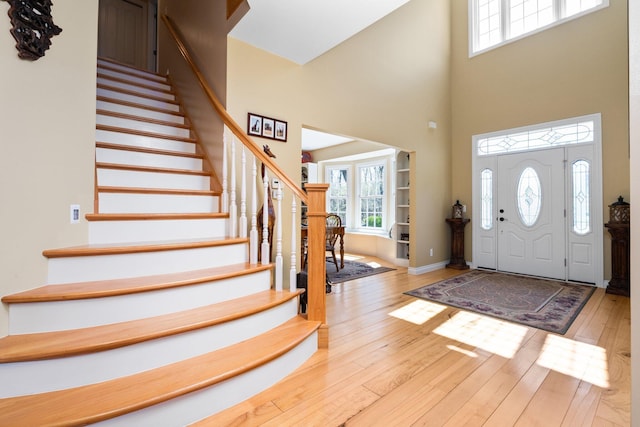 foyer entrance featuring a high ceiling, hardwood / wood-style flooring, stairs, and baseboards