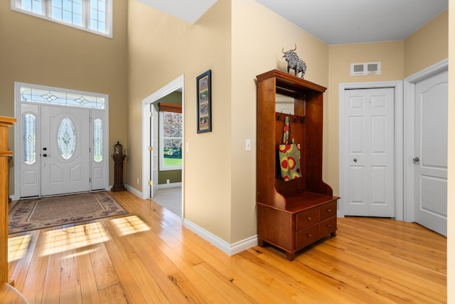 foyer featuring baseboards, visible vents, light wood finished floors, and a towering ceiling
