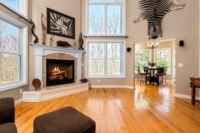 living area featuring wood-type flooring, a towering ceiling, a premium fireplace, and a chandelier