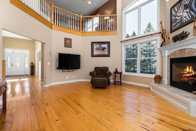 living area featuring a towering ceiling, baseboards, a tiled fireplace, and light wood-type flooring