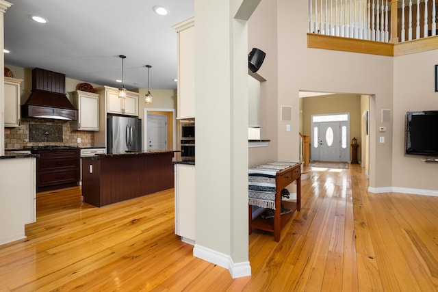 kitchen featuring baseboards, custom exhaust hood, appliances with stainless steel finishes, and light wood finished floors