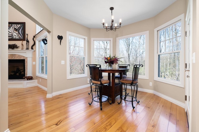 dining area featuring baseboards, an inviting chandelier, light wood-style floors, and a tiled fireplace