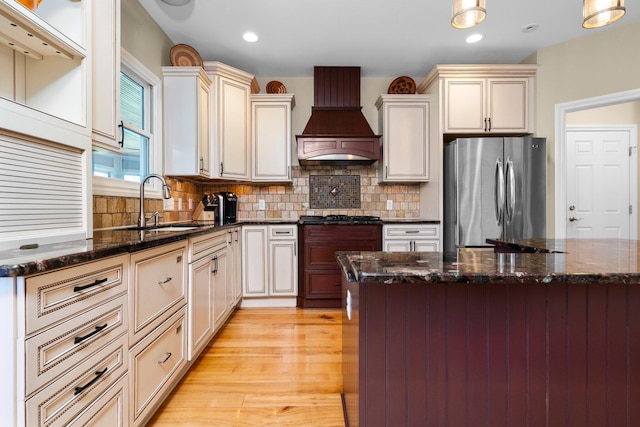 kitchen featuring dark stone counters, custom range hood, a sink, freestanding refrigerator, and backsplash