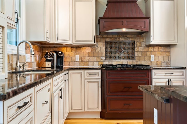 kitchen featuring dark stone countertops, custom range hood, decorative backsplash, and a sink